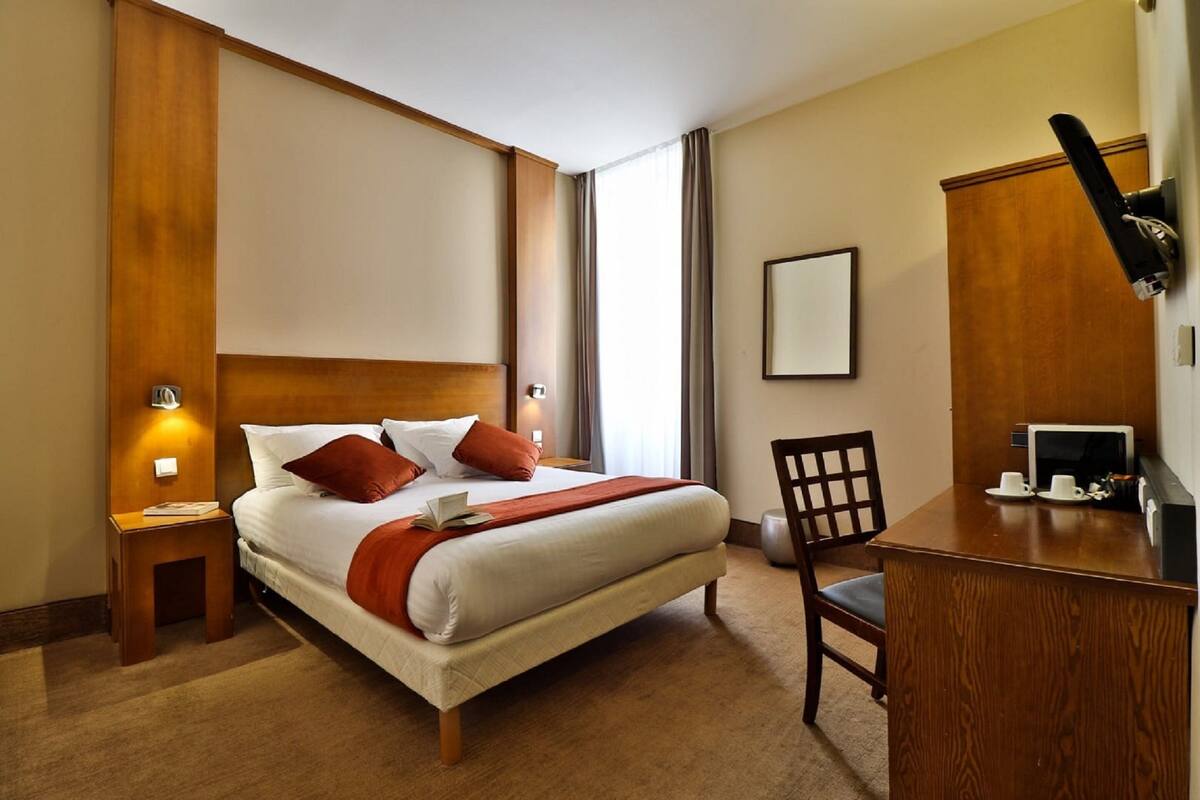 A hotel room with a large bed, a desk, a chair, and a television.