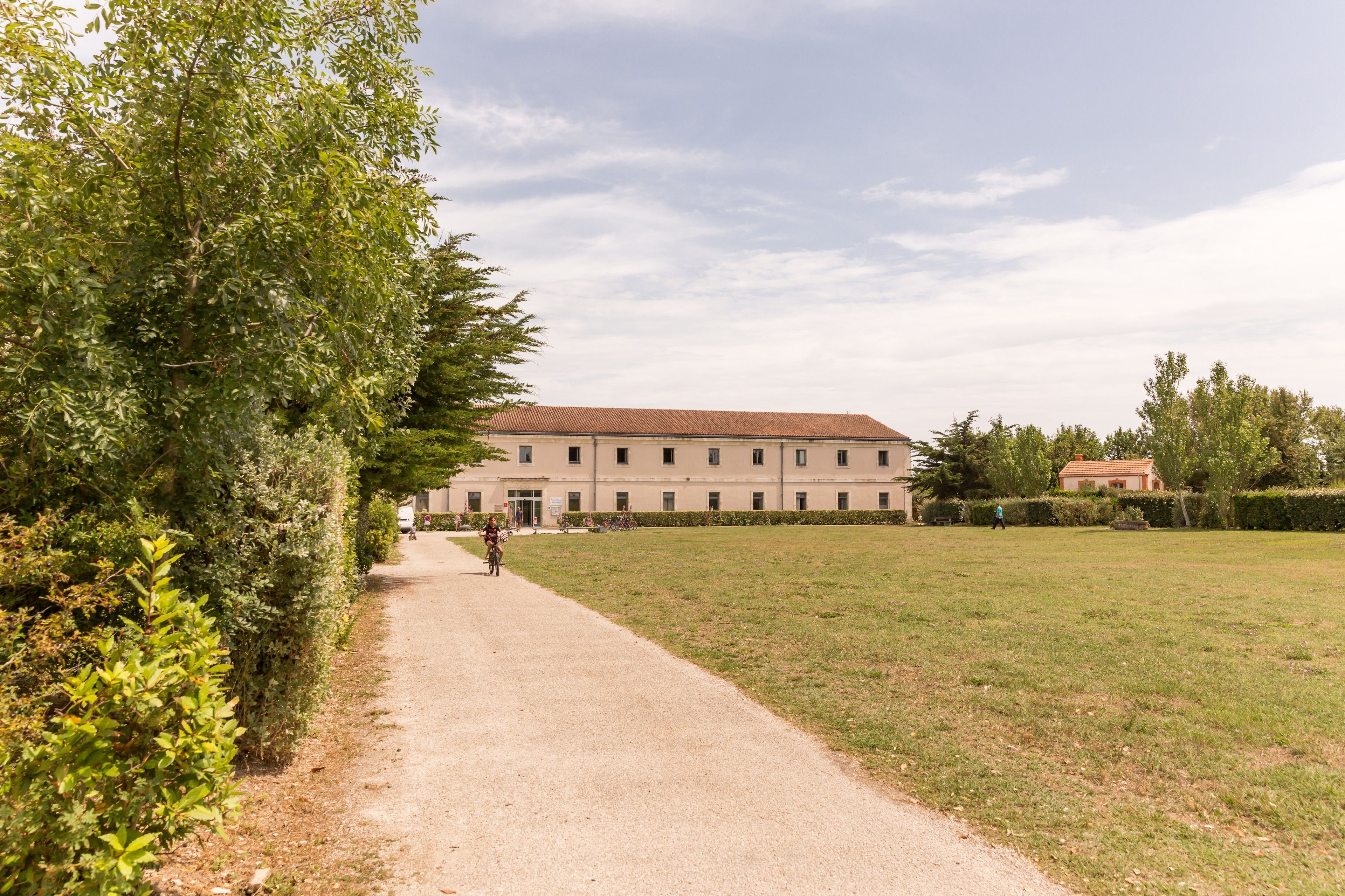 A pathway leading to a building with a red-tiled roof, surrounded by greenery and a clear sky.