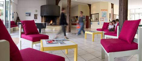 A lobby with red chairs, a fireplace, and a reception desk.