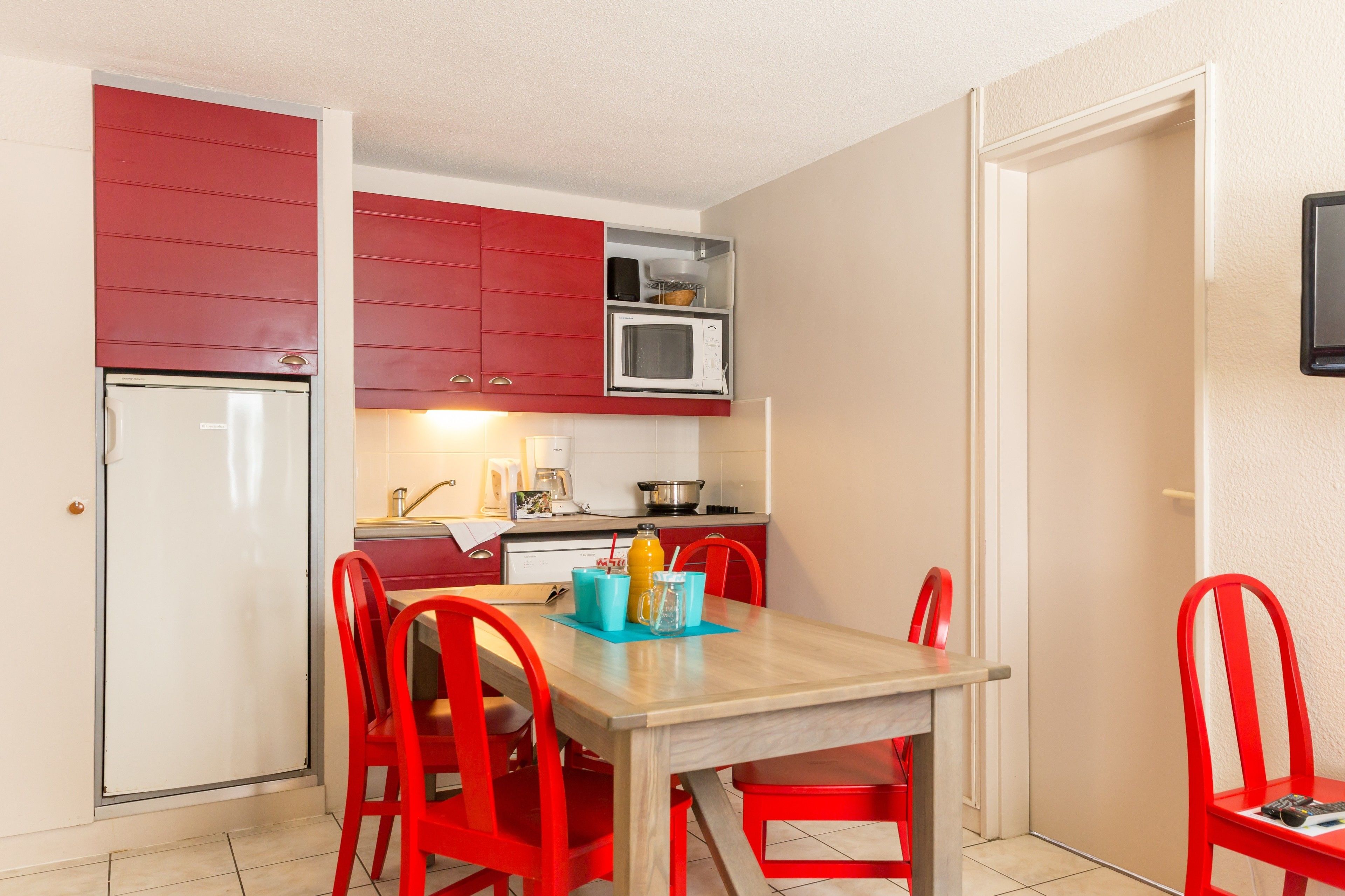 Une cuisine compacte avec des meubles rouges, un four à micro-ondes et un coin repas comprenant une table en bois et des chaises rouges.