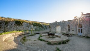 Un pati amb una zona d'estar circular, una taula de picnic i un edifici amb finestres d'arc.