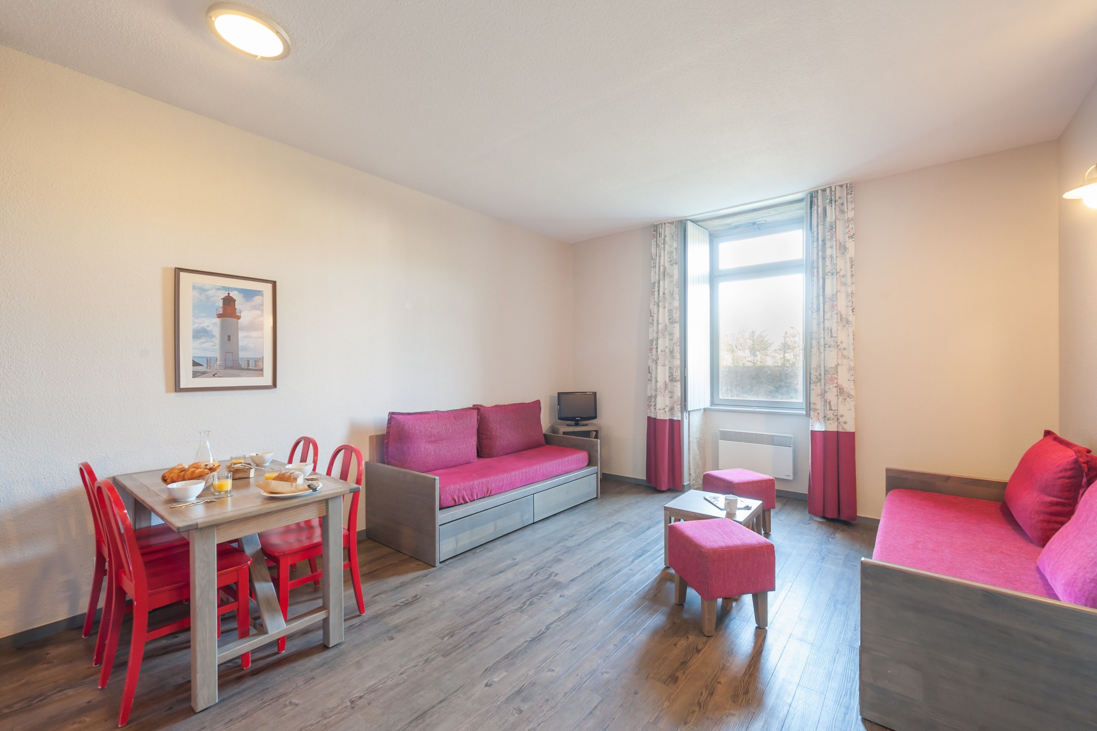 A compact room with a dining table, two sofas, a small TV, and a window with curtains.