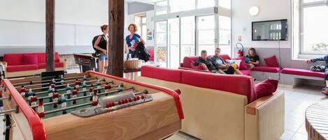 A room with a foosball table, red sofas, and a television.