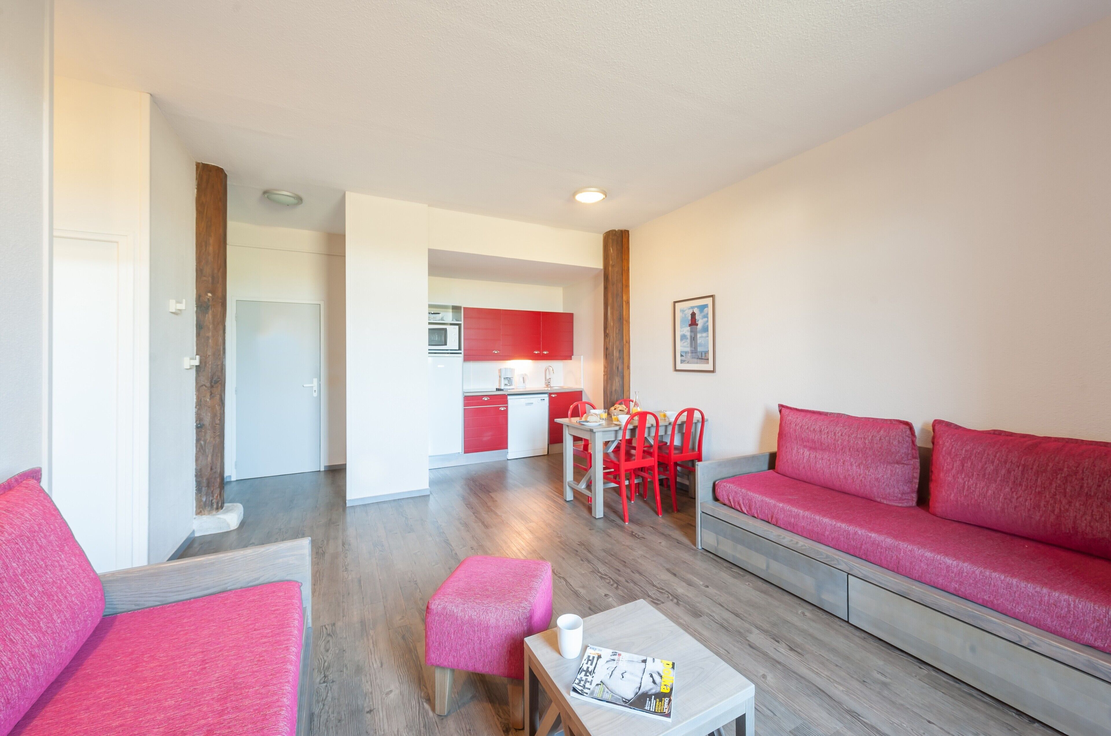 A modern living room with a red sofa, a small table, and a dining area with red chairs.
