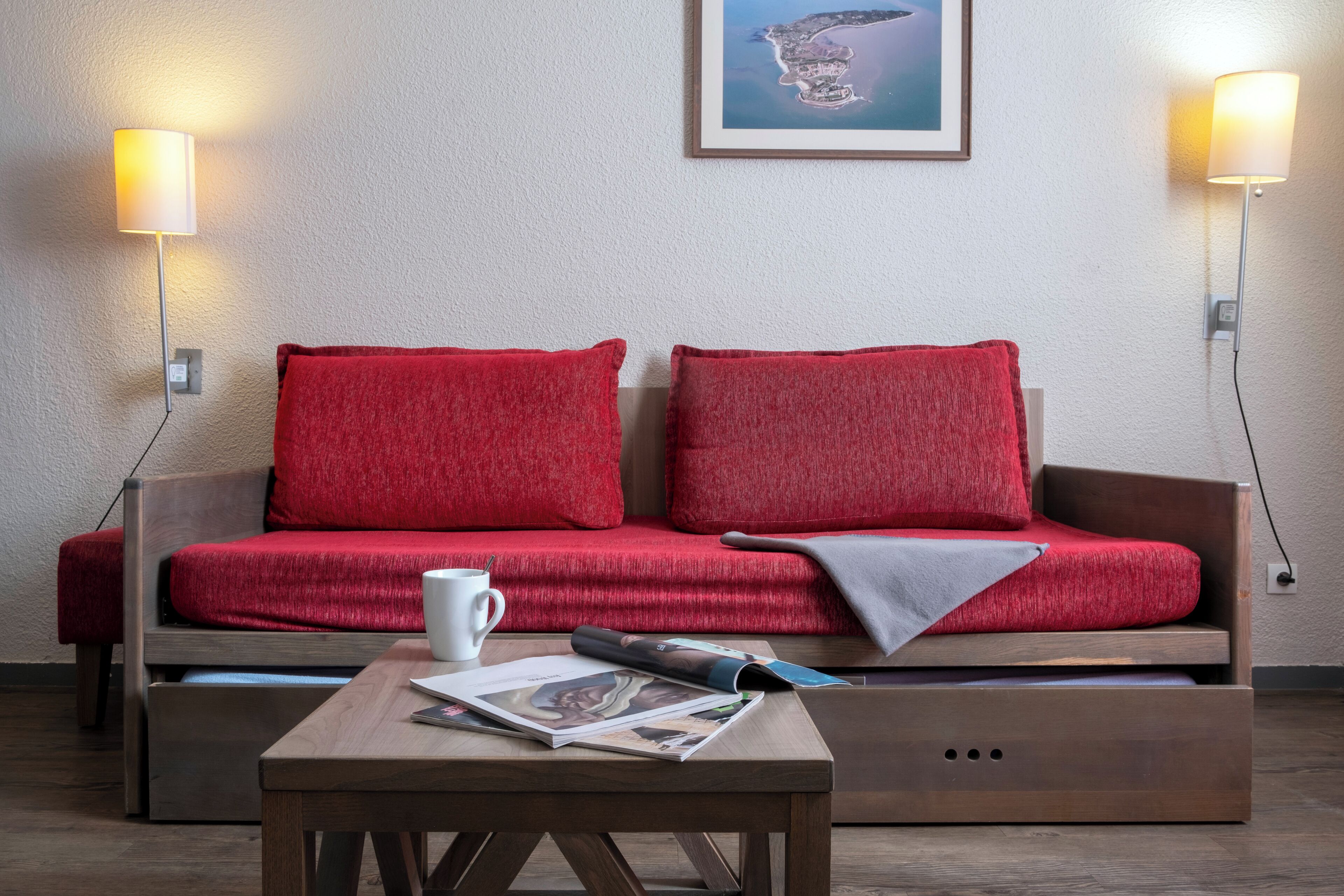 Ein modernes Zimmer mit einer Holzsofa, roten Kissen, einem Couchtisch mit einer Zeitschrift und zwei Wandlampen.