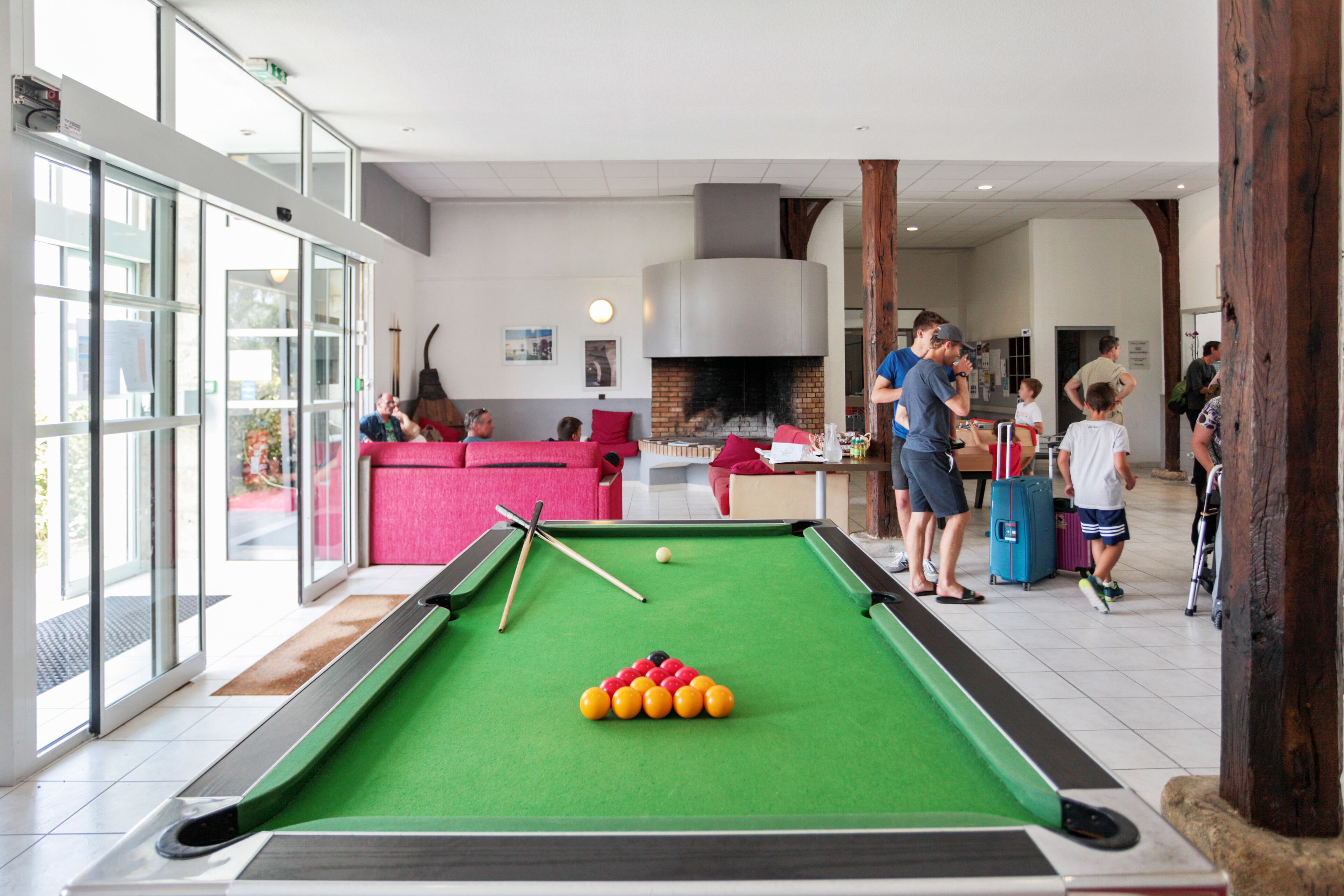 A pool table in a well-lit indoor space with a fireplace, a sofa, and a kitchen area.