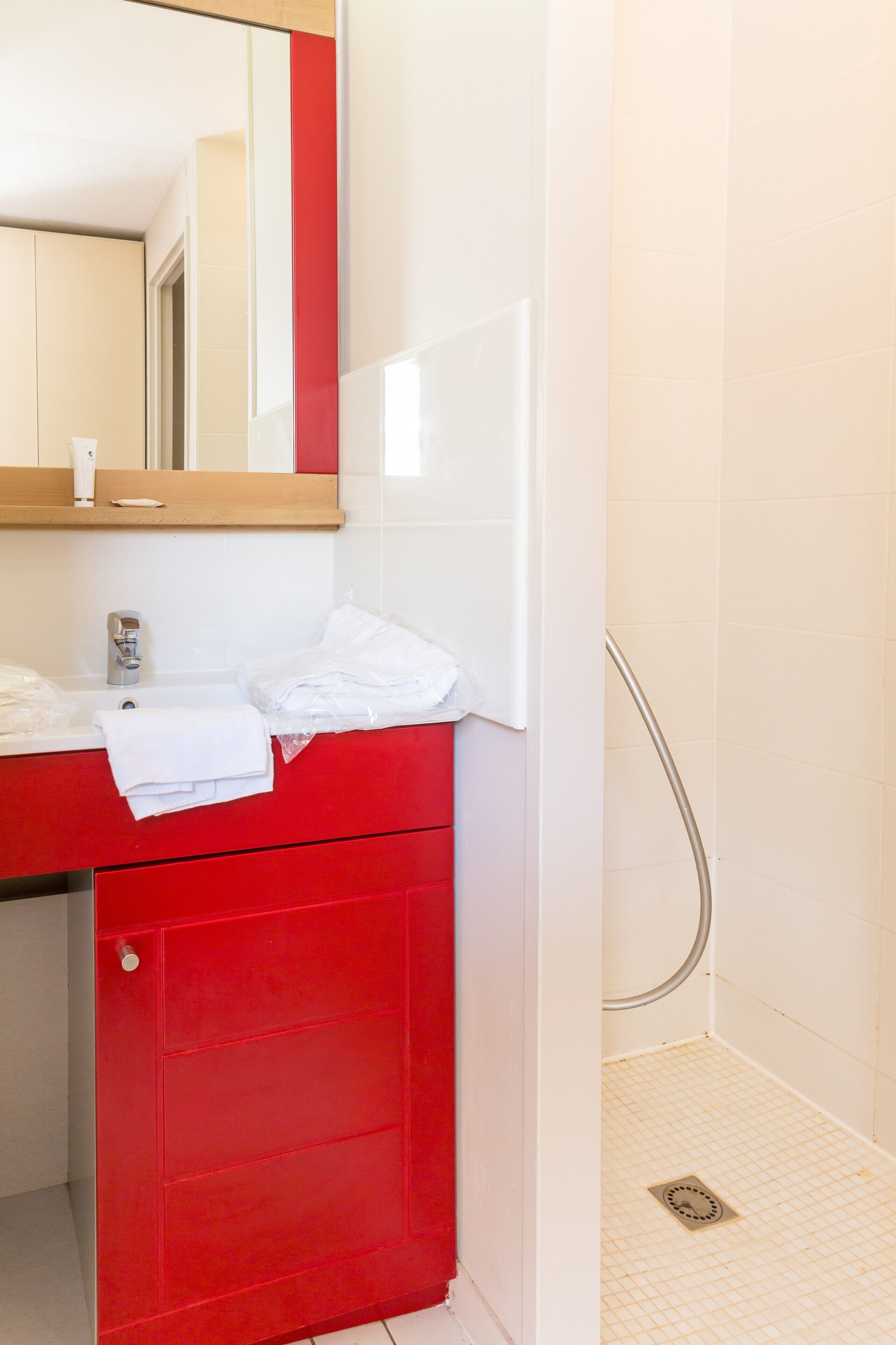 A bathroom with a red vanity, a mirror, a white sink, and a shower area.