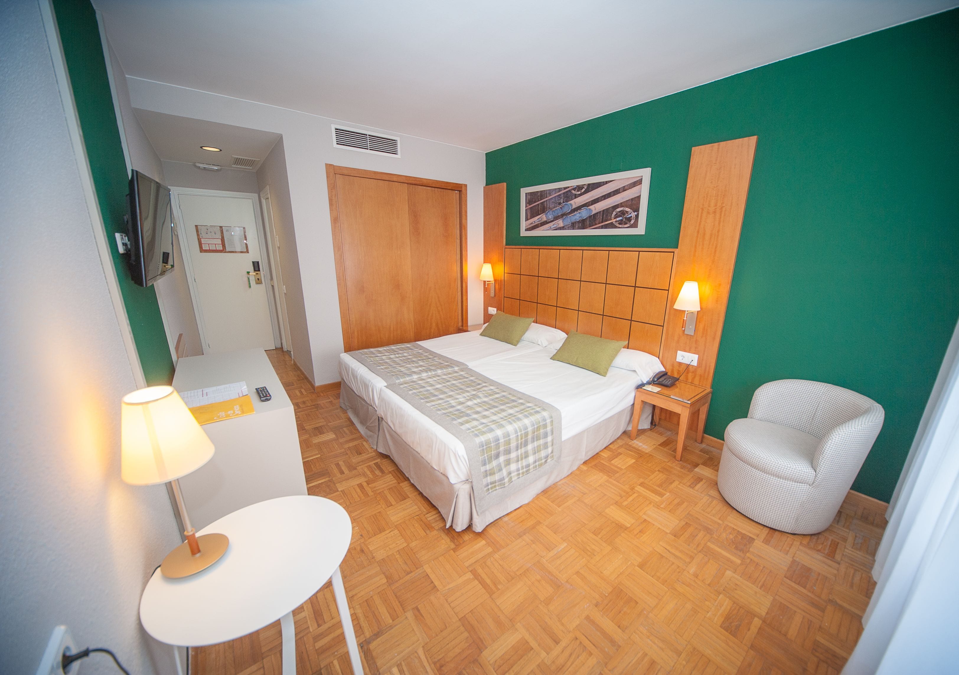 Une chambre d’hôtel avec un lit, des tables de chevet, une chaise, un téléviseur et un mur vert.