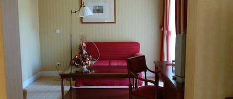 Un salon avec un canapé rouge, une table basse en bois, un fauteuil, une lampe et un tableau encadré accroché au mur.