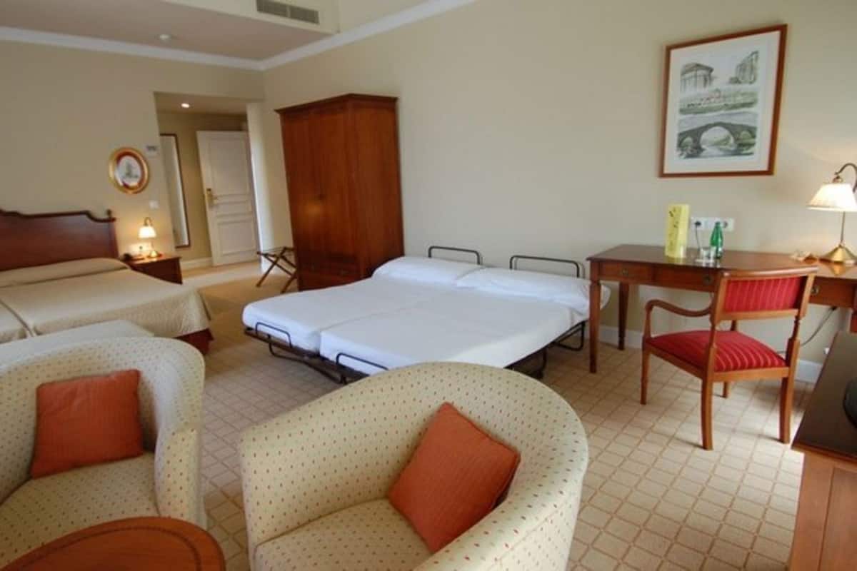 Habitación de hotel con dos camas, un escritorio, una silla, un armario y un cuadro en la pared.