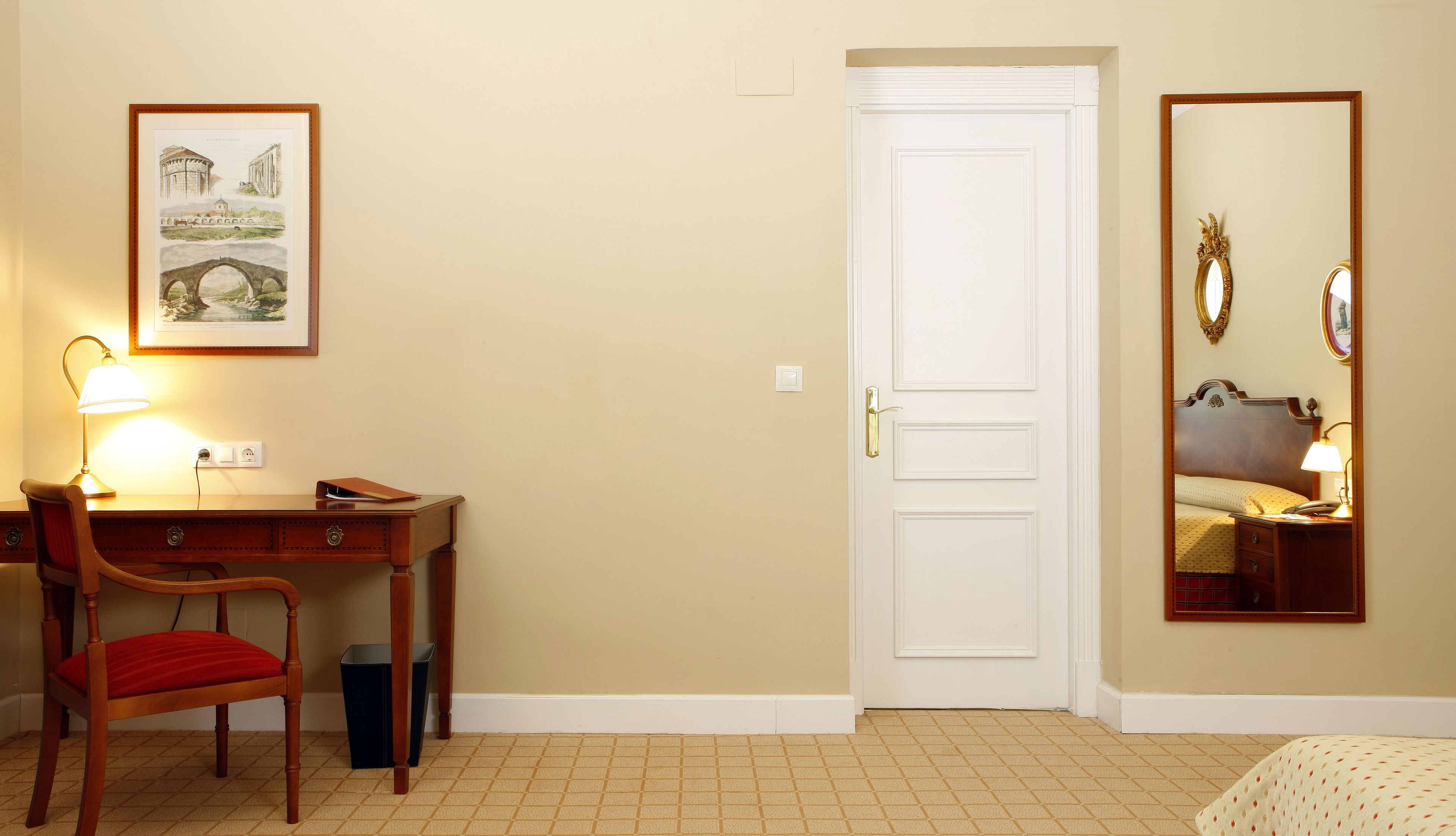 Habitación de hotel con escritorio, silla, lámpara y un espejo grande.