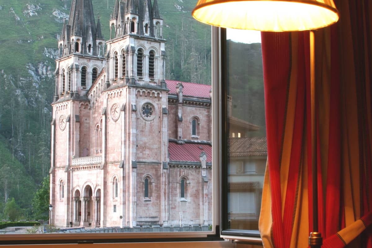 Una ventana con vista a una iglesia histórica de dos torres y un campanario.