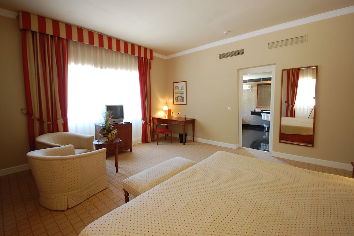 Habitación de hotel con dos camas, un escritorio, una silla y un baño visible a través de una puerta abierta.
