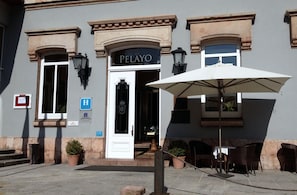 The exterior of the Pelayo hotel with a white entrance, outdoor seating area, and potted plants. - Gran Hotel Pelayo (Cangas de Onis)