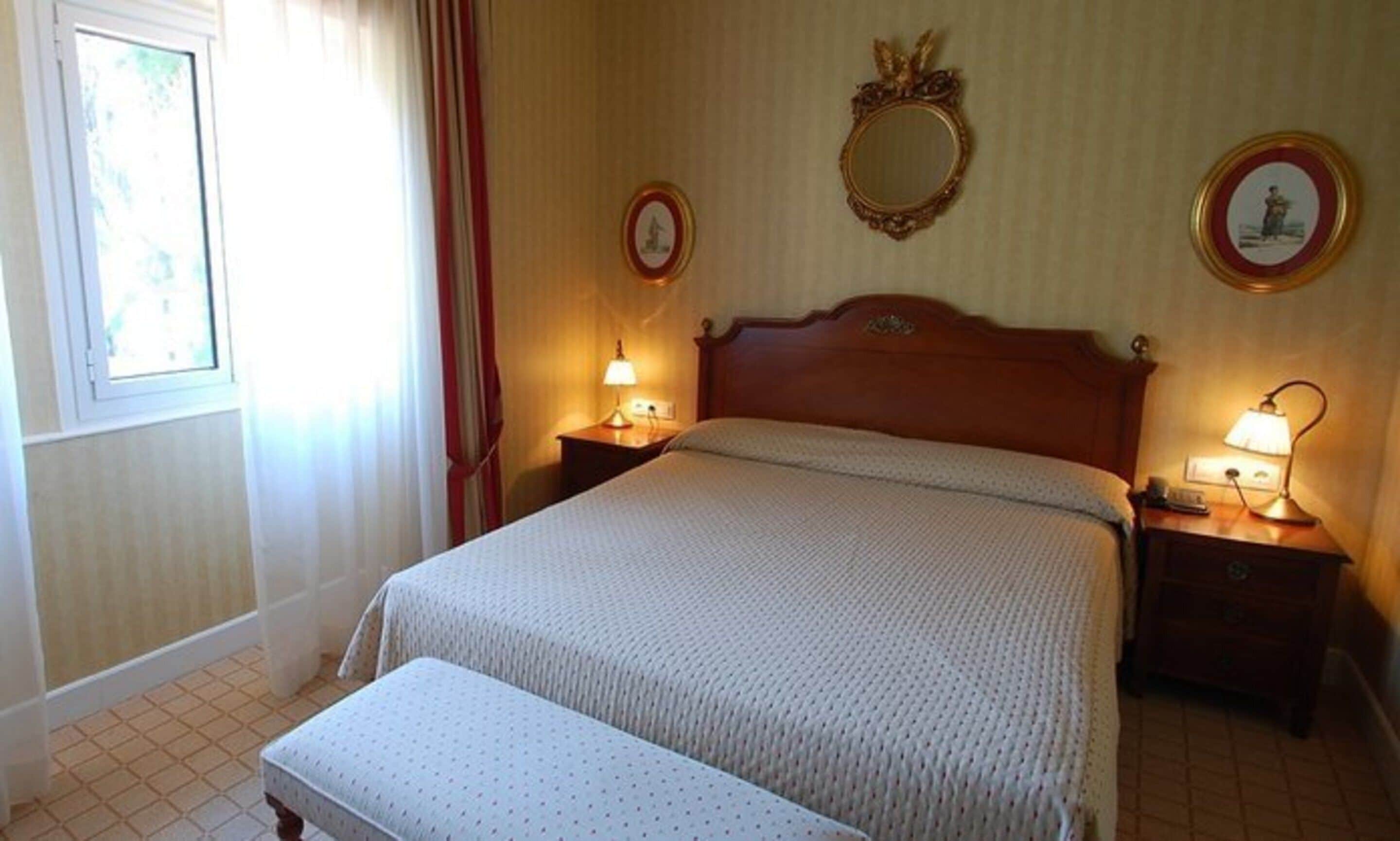 A neatly made bed with a wooden headboard, two bedside tables with lamps, a mirror, and a framed picture on the wall.