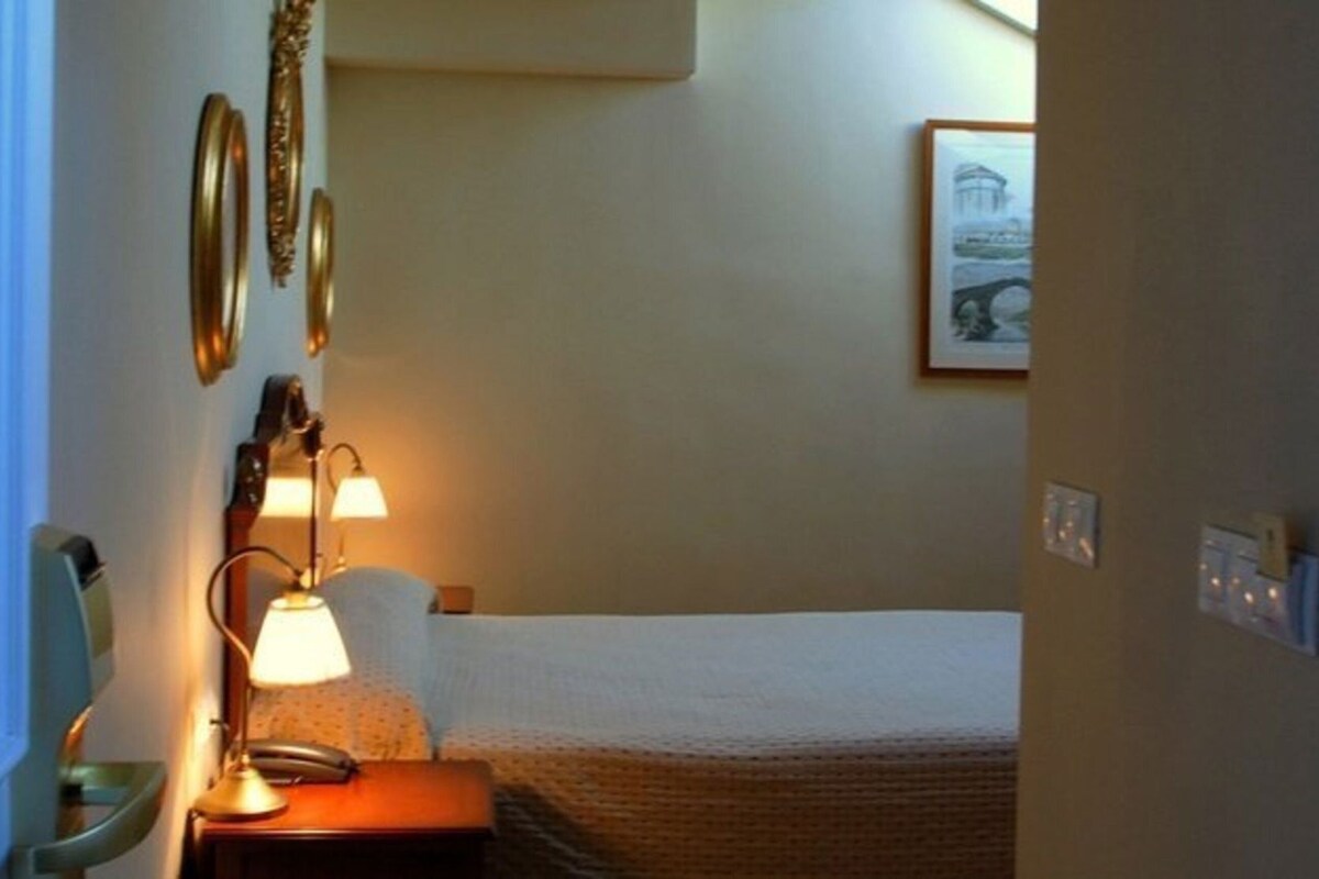 A hotel room with a bed, a bedside lamp, a telephone, and a framed picture on the wall.