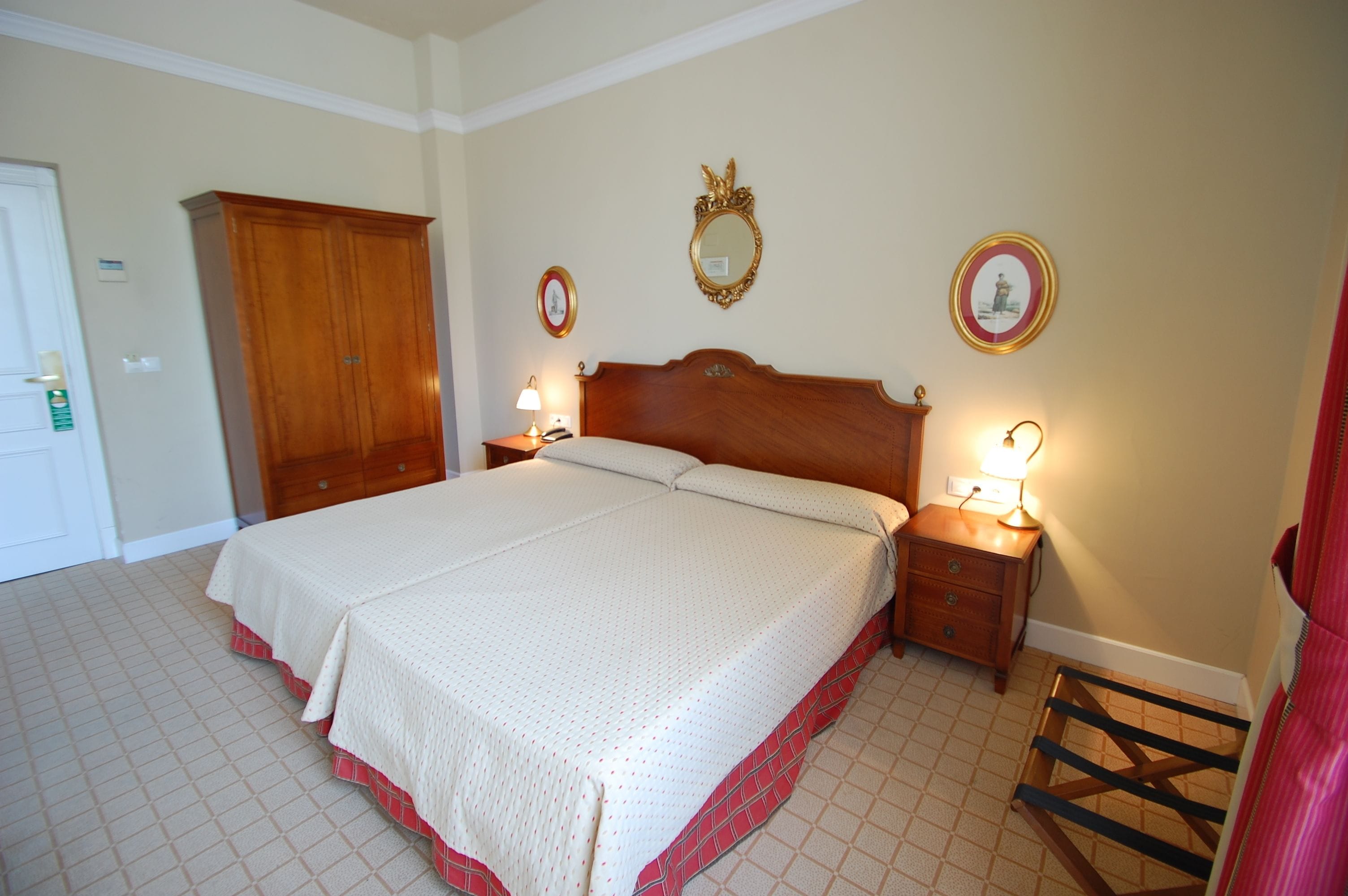 A neatly arranged bedroom with a large bed, bedside tables with lamps, a wardrobe, and a mirror on the wall.