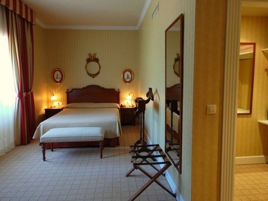 Una habitación de hotel con una cama grande, dos mesitas de noche con lámparas, un espejo y un armario.