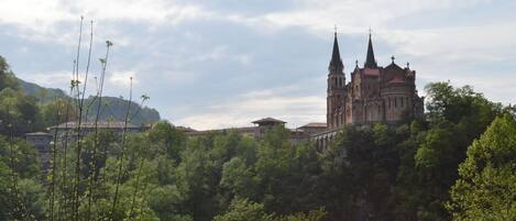 Una iglesia histórica con dos torres gemelas, rodeada de exuberante vegetación y colinas.