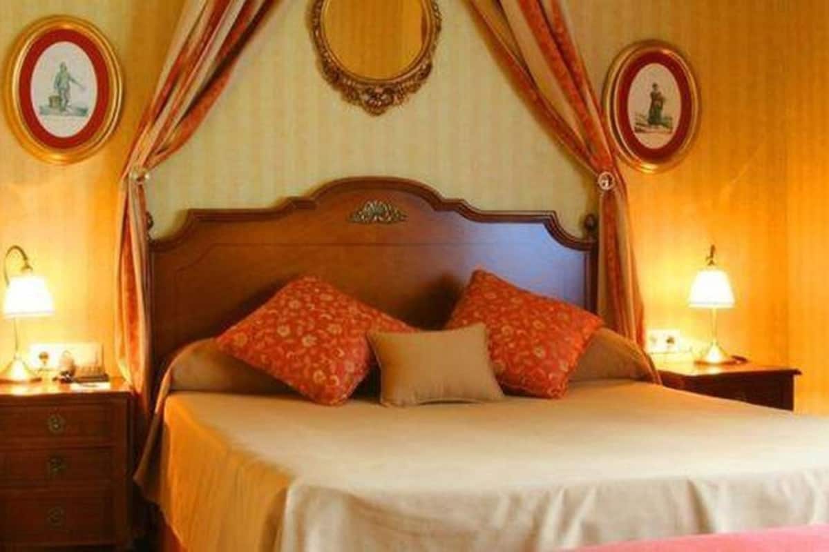 Una cama con cabecera de madera, dos mesitas de noche con lámparas, y dos cuadros colgados en la pared.