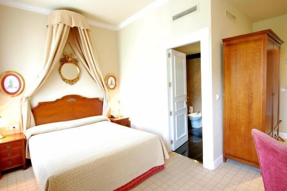 A bedroom with a bed, bedside tables, a wardrobe, and a bathroom visible through an open door.