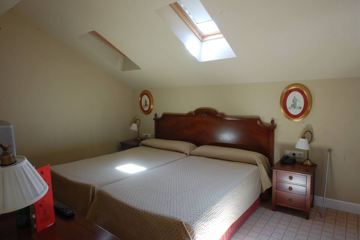 Un dormitorio con cama, mesitas de noche, lámpara, reloj de pared y tragaluz.