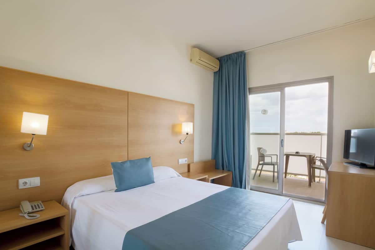 Une chambre d’hôtel avec un grand lit, des lampes de chevet, un bureau, une télévision et un balcon équipé d’une table et de chaises.