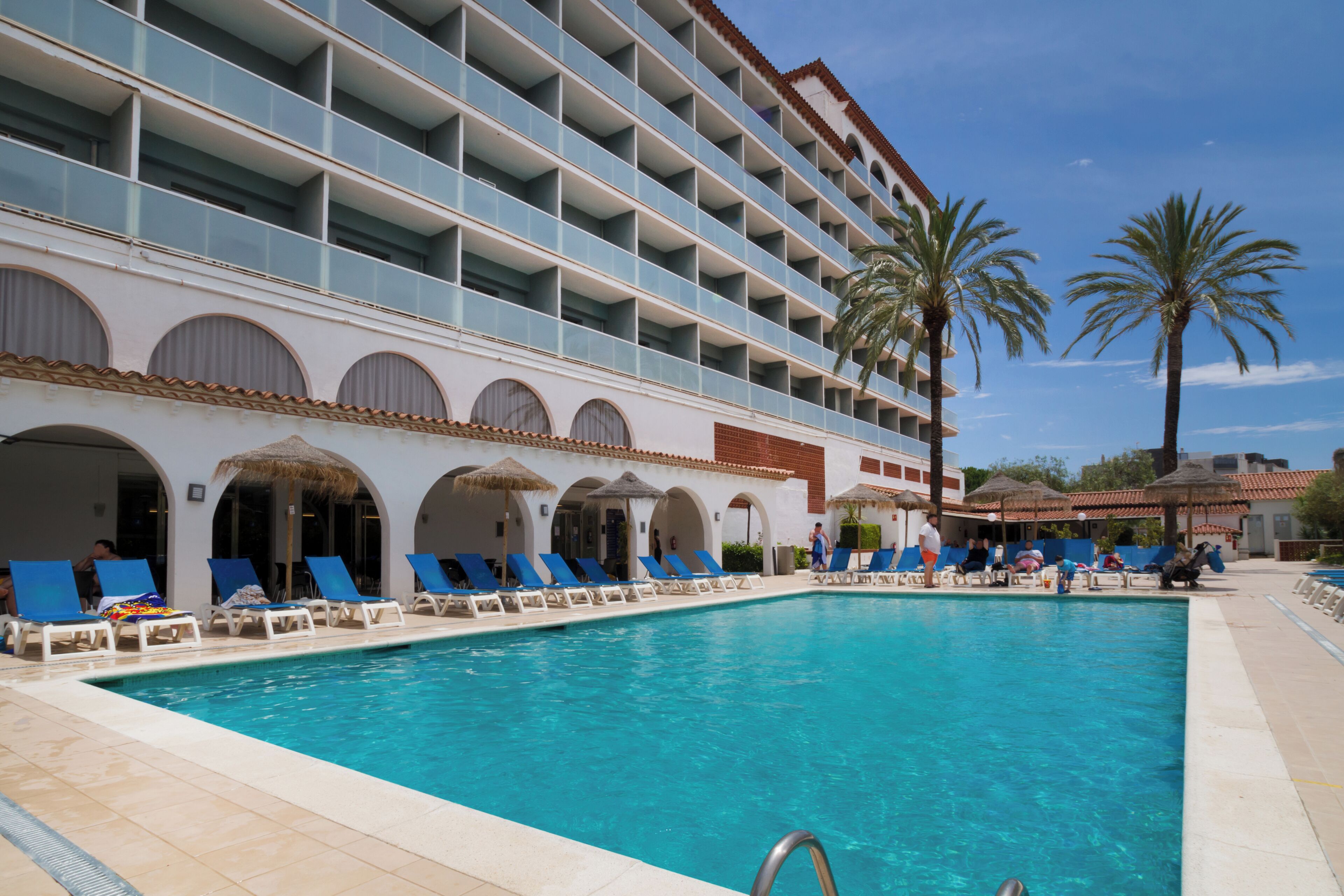 Ein Hotelpoolbereich mit mehreren Balkonebenen, Liegestühlen und Palmen.