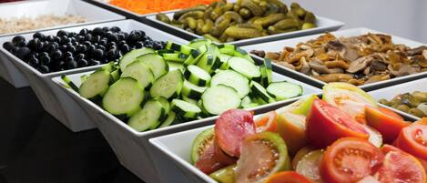 Un bufé con diversos alimentos, entre ellos aceitunas, pepinos, tomates y encurtidos.