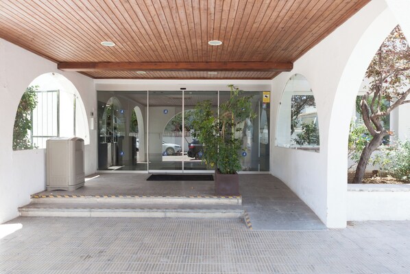 Entrada de un edificio con techo de madera, puertas de vidrio y una planta en maceta.