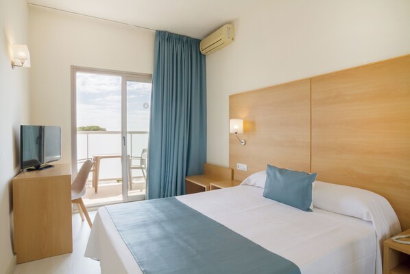 Habitación de hotel con una cama grande, un escritorio con televisor, una silla y vistas al exterior a través de una puerta corrediza.