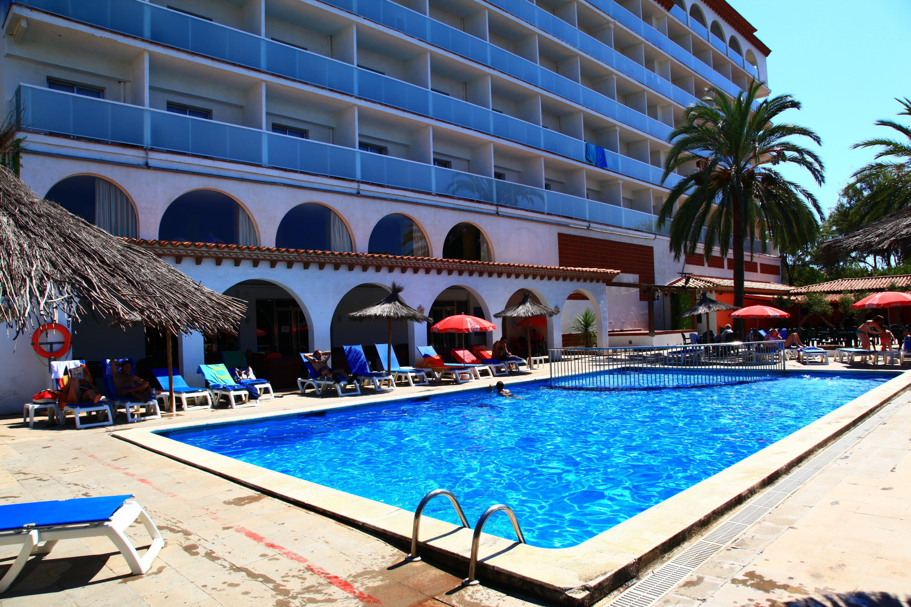 Un albergo con piscina, poltrone a sdraio e ombrelloni.