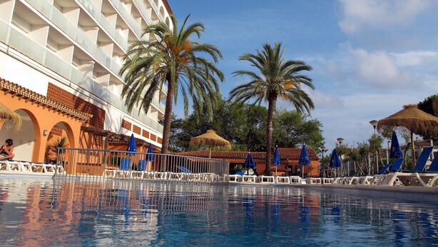 Un hotel con piscina, palmeras y cielo despejado.