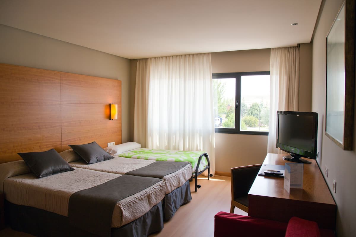 A hotel room with two beds, a desk with a television, and a window with curtains.