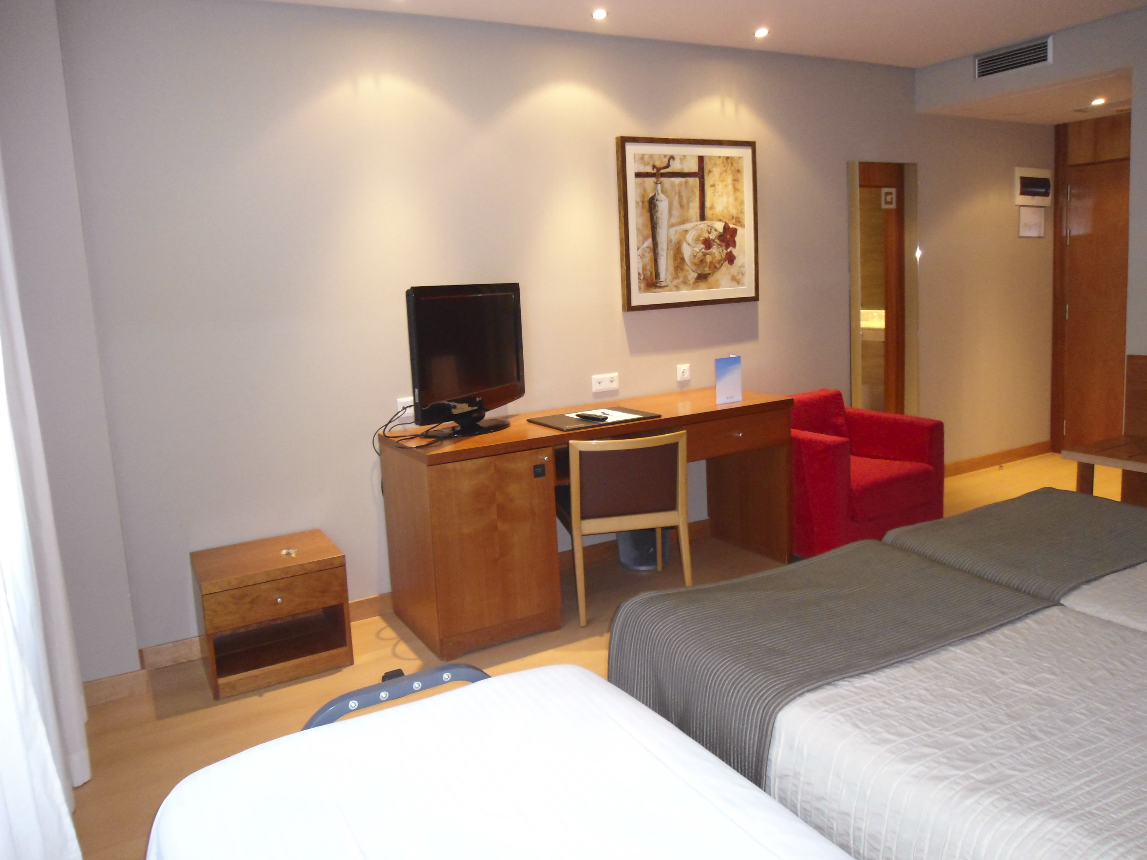 Habitación de hotel con una cama, un escritorio con computadora, una silla y un sillón rojo.