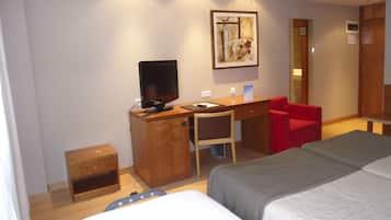 Habitación de hotel con una cama, un escritorio con computadora, una silla y un sillón rojo.
