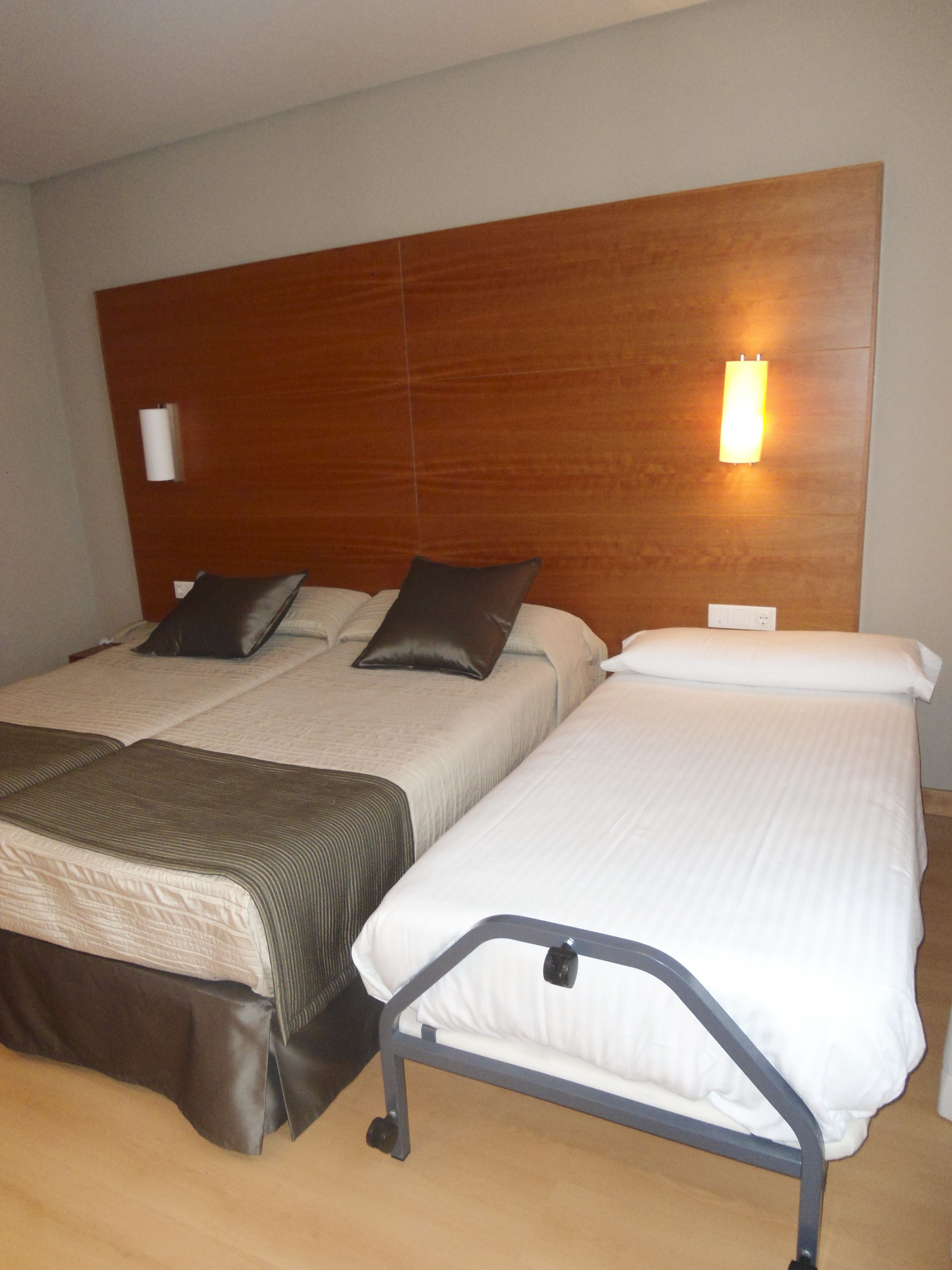 A hotel room with two beds, each with a headboard, and a bedside table.