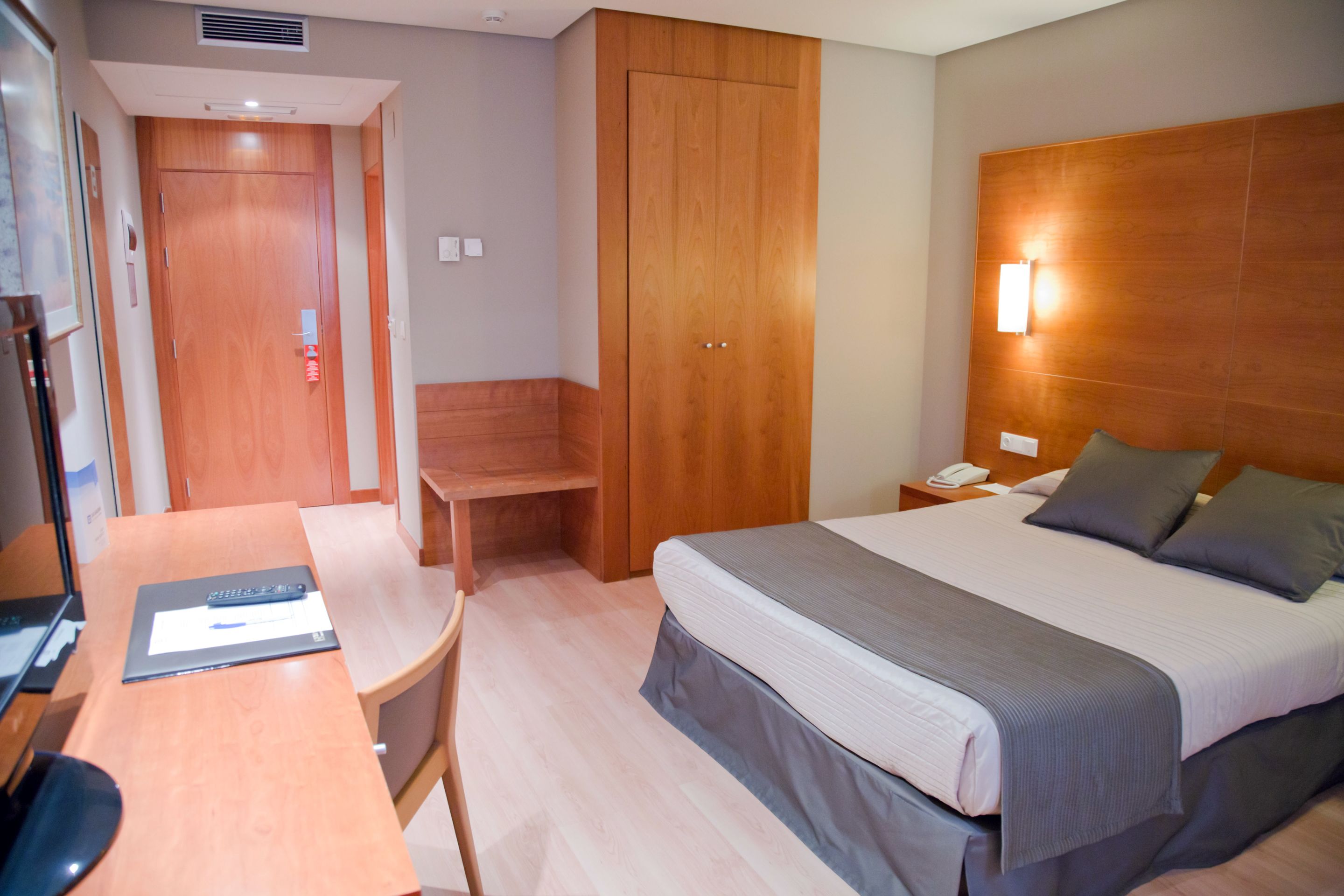 Una habitación de hotel con cama, mesita de noche, silla, escritorio y armario.