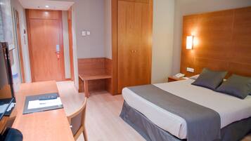 Una habitación de hotel con cama, mesita de noche, silla, escritorio y armario.