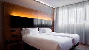 A double bed with white linens, a wooden headboard, a flat-screen TV, and a nightstand with a power outlet.