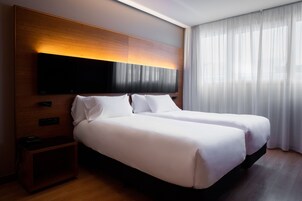 Un lit double avec du linge de lit blanc, une tête de lit en bois, un téléviseur à écran plat et une table de chevet équipée d’une prise électrique.
