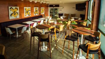 Um restaurante com várias mesas e cadeiras, uma televisão fixada na parede e obras de arte nas paredes.