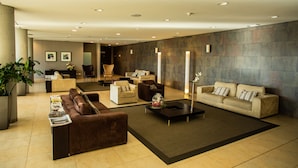 A modern lobby with a brown sofa, beige armchairs, a coffee table, and a large potted plant.
