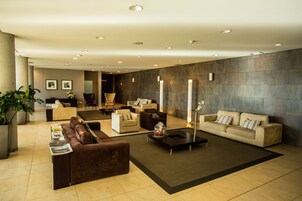 Un hall d’entrée moderne avec un canapé marron, des fauteuils beige, une table basse et une grande plante en pot.