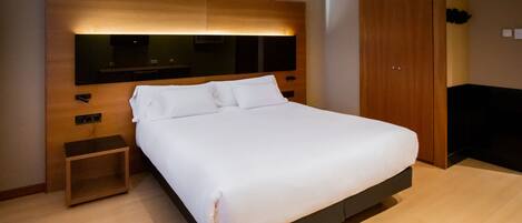 A modern hotel room with a large bed, a wooden headboard, a small bedside table, and a built-in TV.