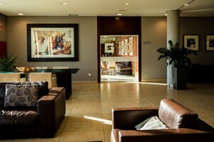 Un hall d’entrée spacieux au design moderne, avec des canapés en cuir, un grand tableau abstrait et un espace café bien visible.
