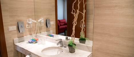 A modern bathroom with a marble sink, a large mirror, and a decorative plant.