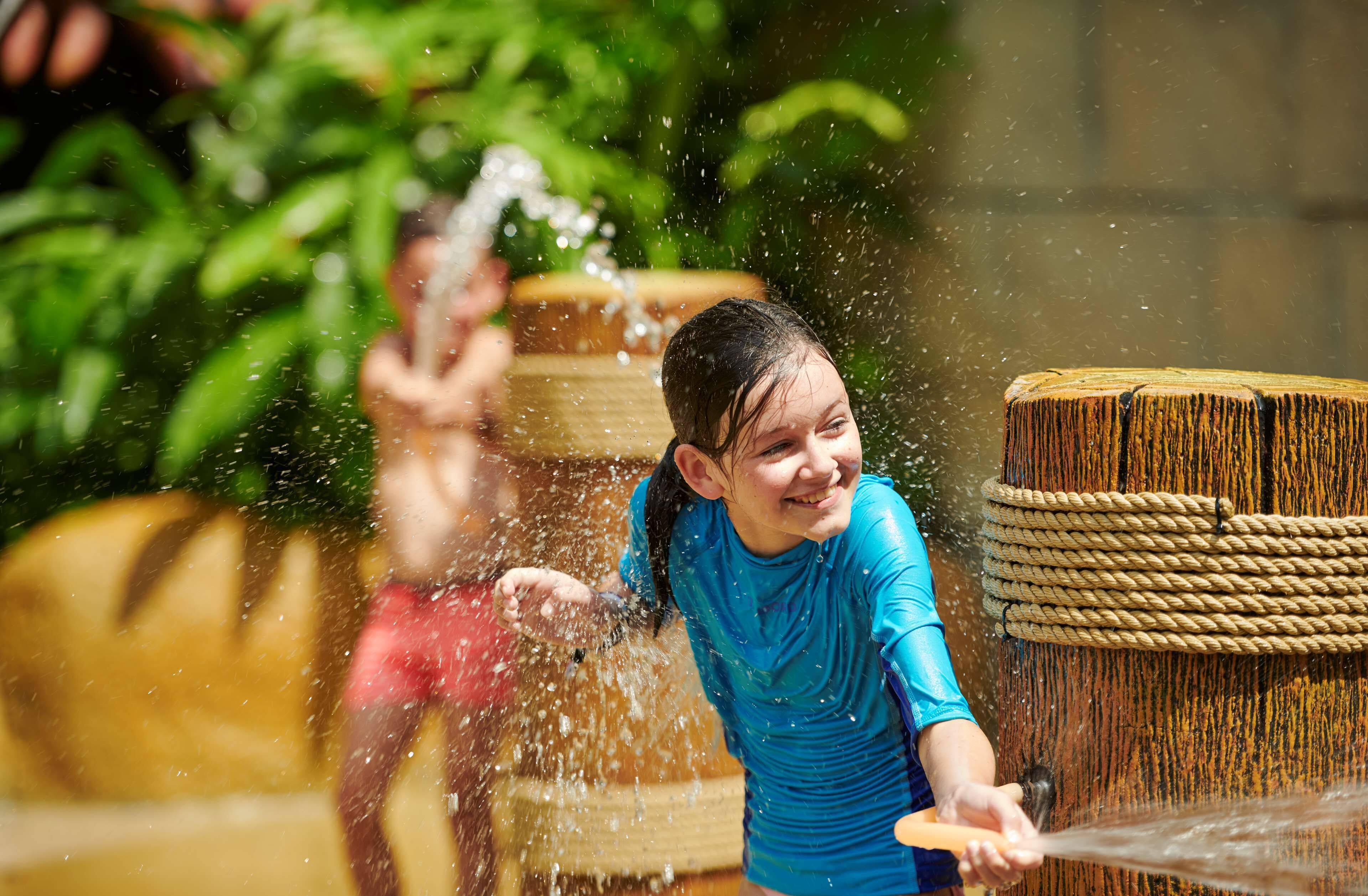 A child playing with water in a wooden barrel.