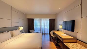 A modern hotel room with a large bed, a desk, a chair, and a TV.