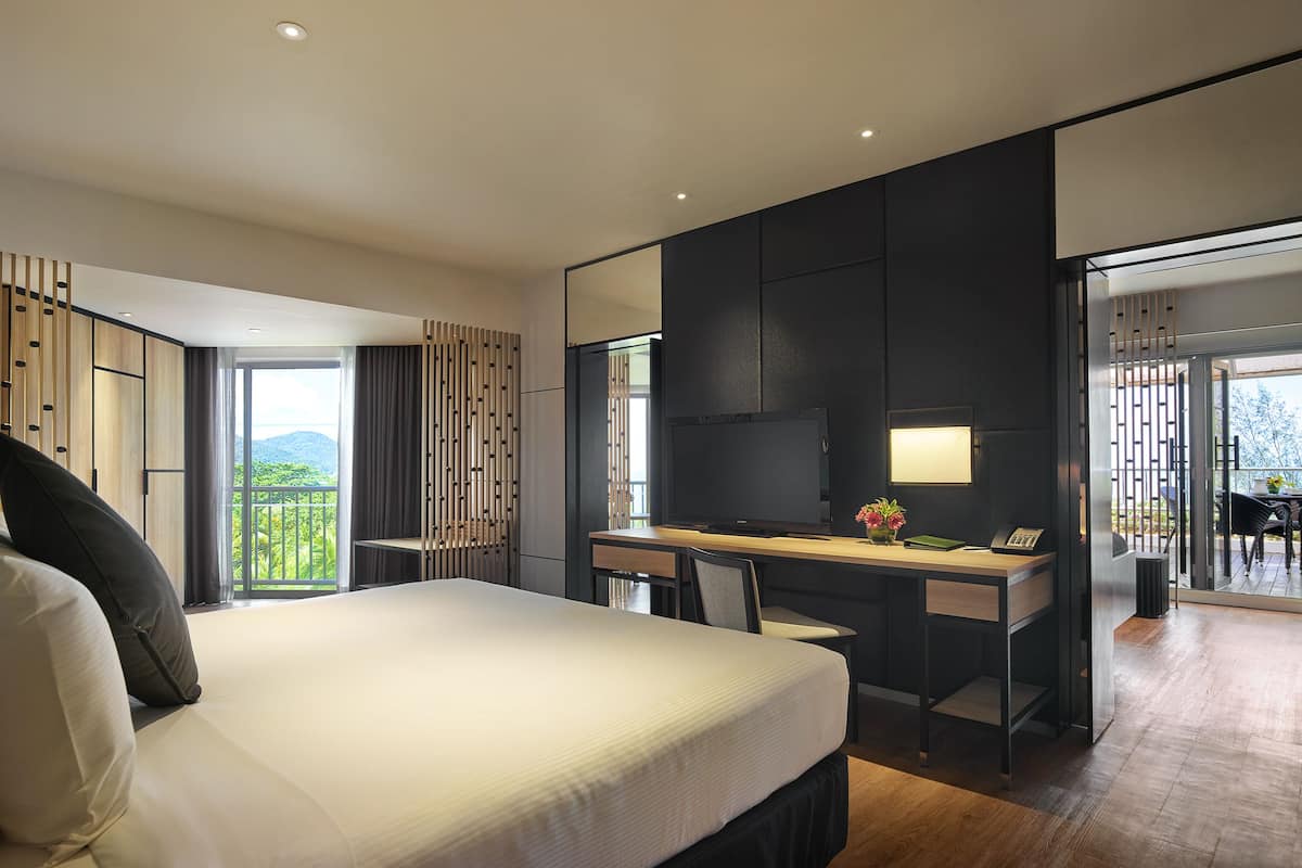 A modern hotel room with a large bed, a desk, and a balcony with a view of the mountains.
